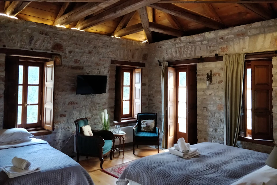 Quarto com paredes de pedra, duas camas e poltronas junto à janela