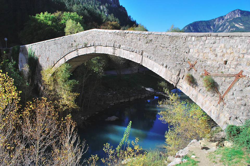 Ponte de pedra de um só arco sobre um ribeiro entre árvores