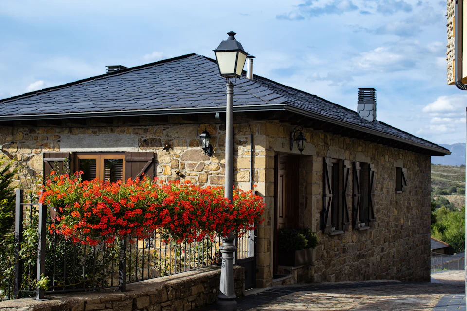 Casa de pedra com gerânios vermelhos na varanda e telhado de lousa